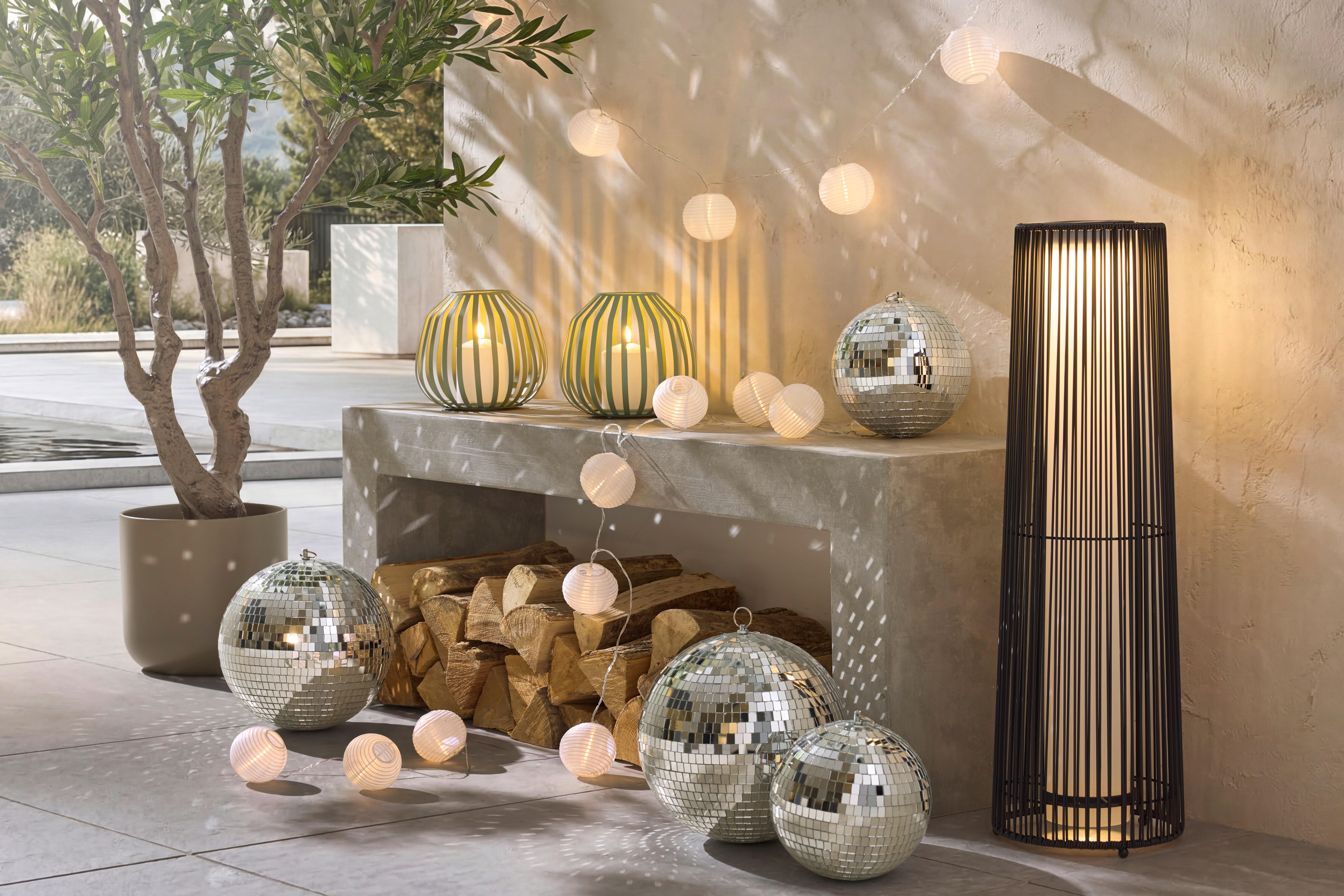 Solárne a dekoratívne svetlá na terase pri krbe, doplnené zrkadlovými guľami pre jemnú večernú atmosféru.