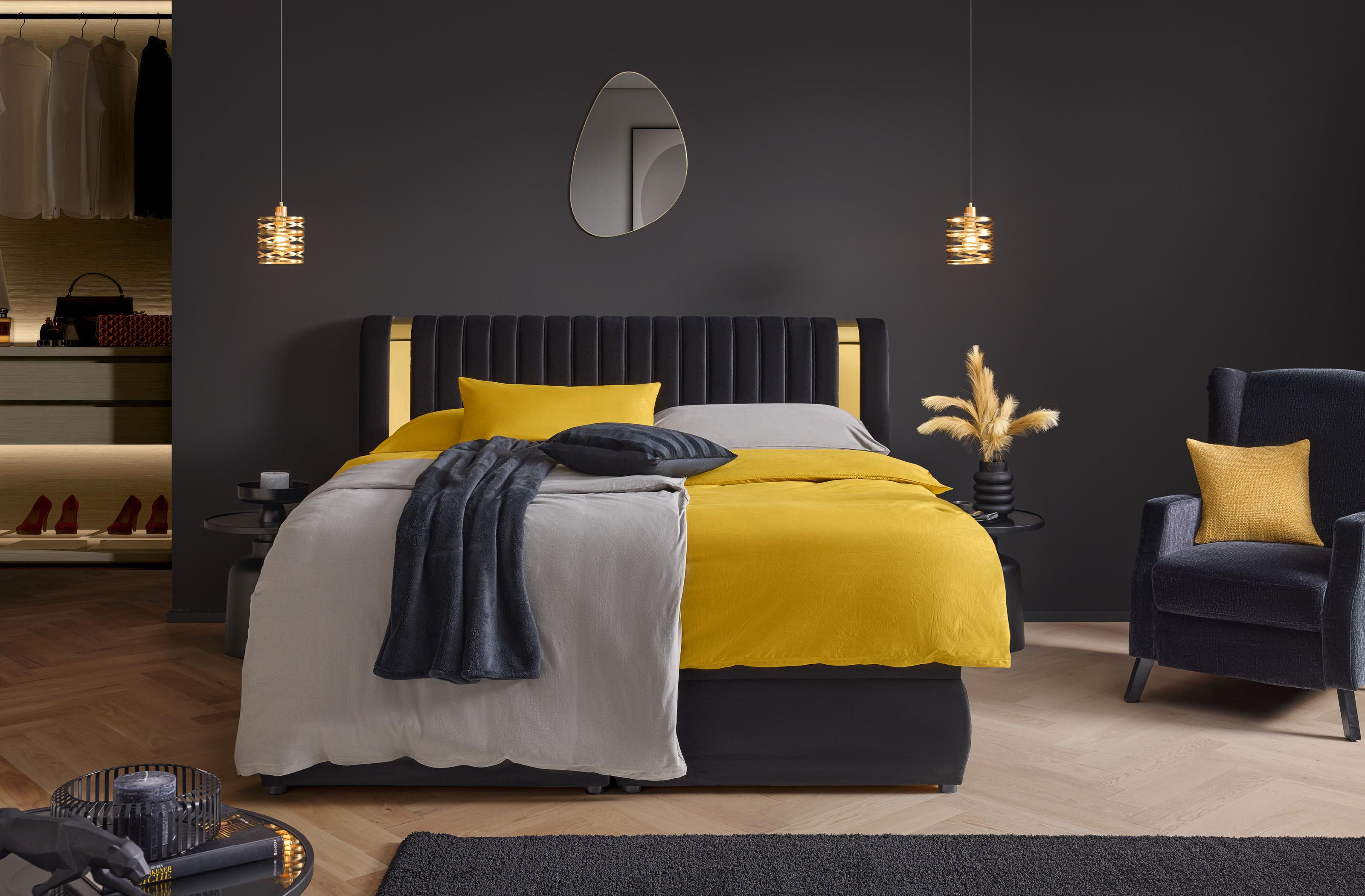 Luxusná spálňa Golden Dreams: čierne lôžko so zlatými detailmi, žlté obliečky Ornament a štýlové dekorácie pre dokonalý oddych.
