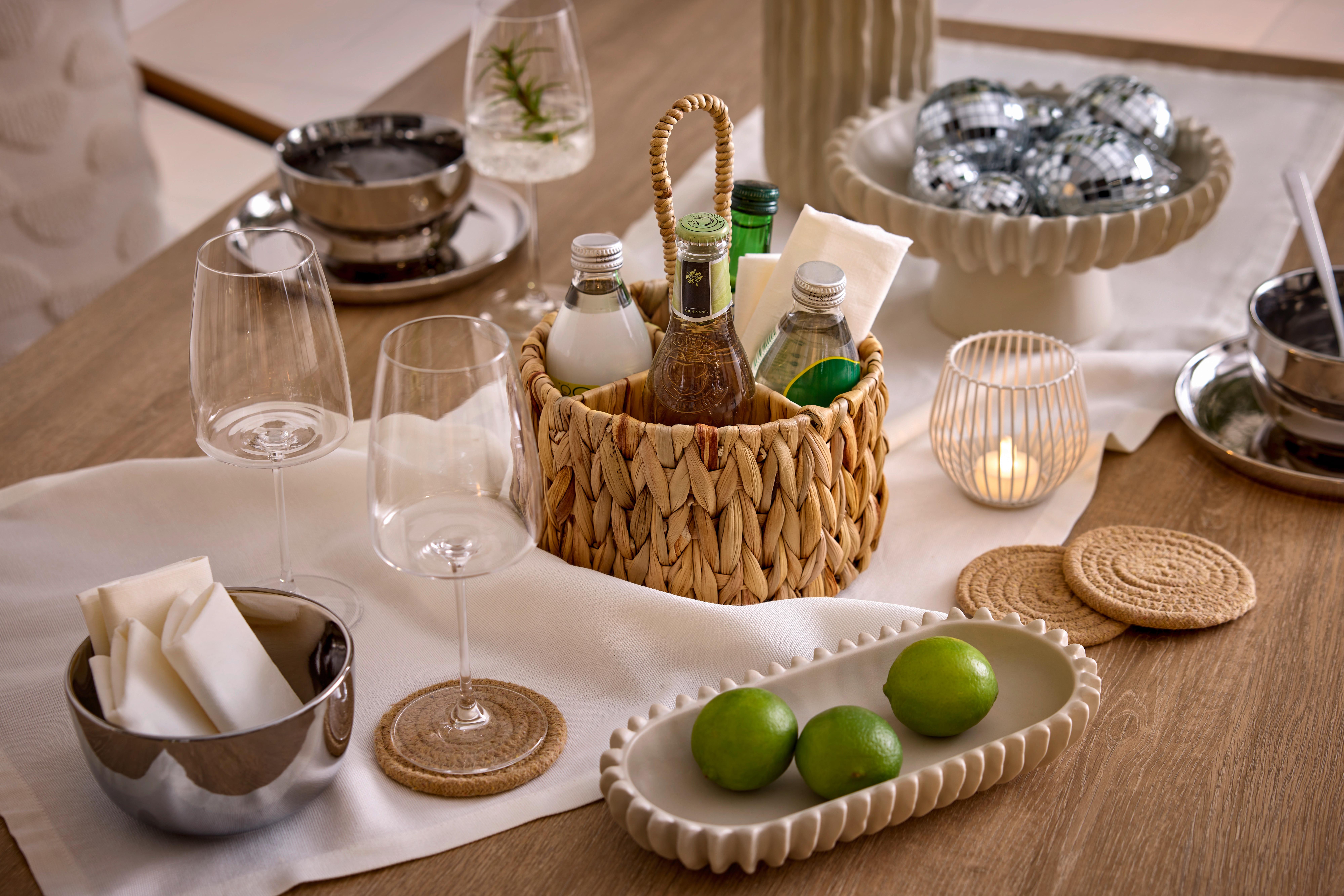 Detail prestretého stola s pleteným košíkom na nápoje, pohármi, svietnikom a miskou s limetkami.