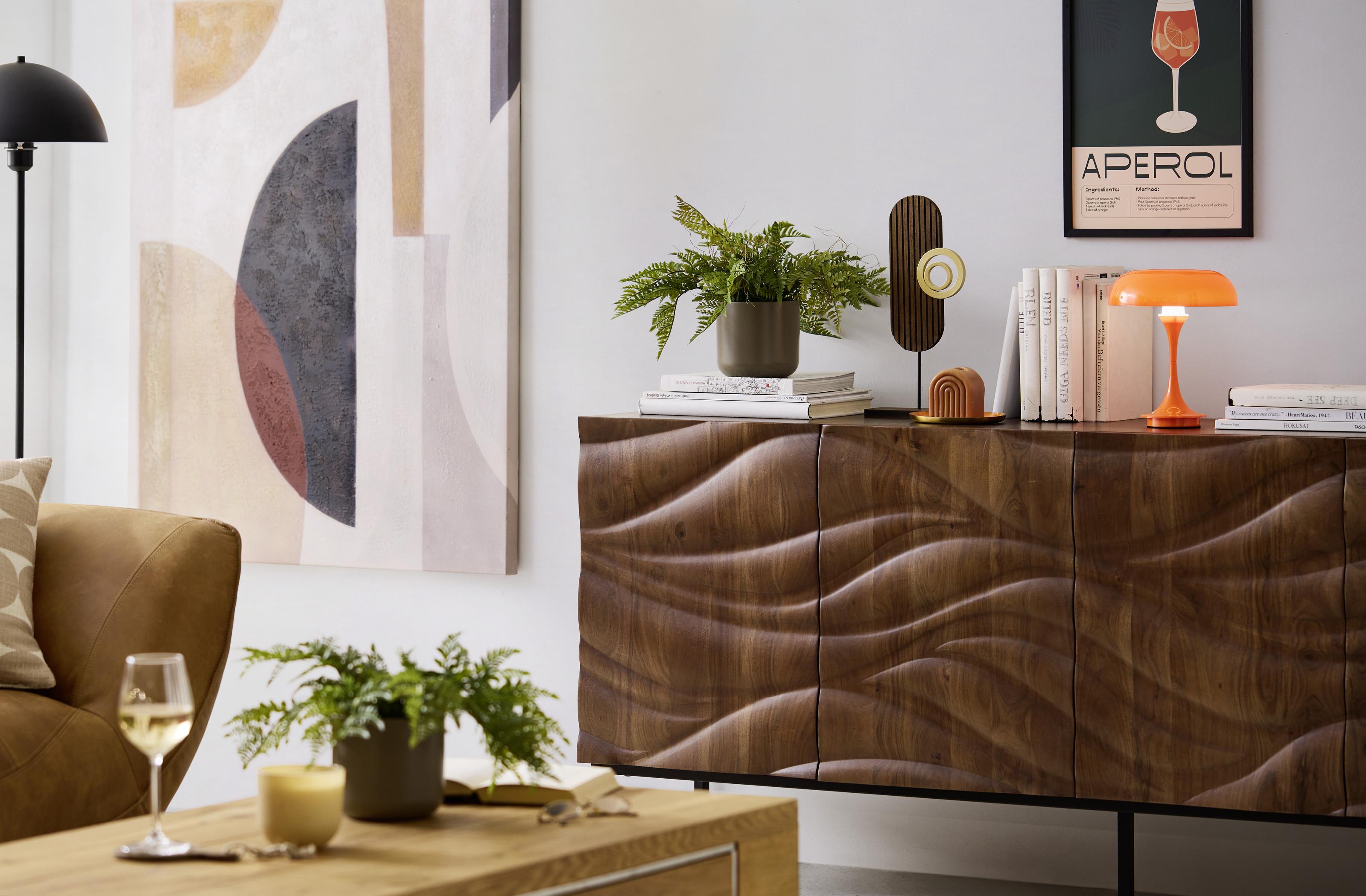 Drevená retro komoda s plastickým vzorom doplnená o dekorácie, izbové rastliny a moderné osvetlenie v štýlovej obývačke.