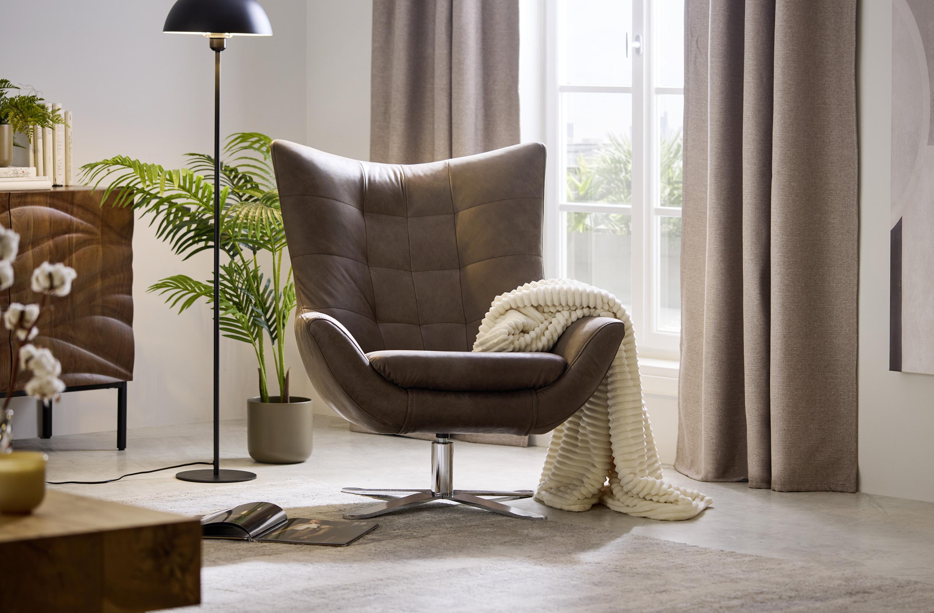 Retro kreslo v útulnom svetlom interiéri s dekou, prírodnými textúrami a zeleňou ako ideálne miesto na oddych.