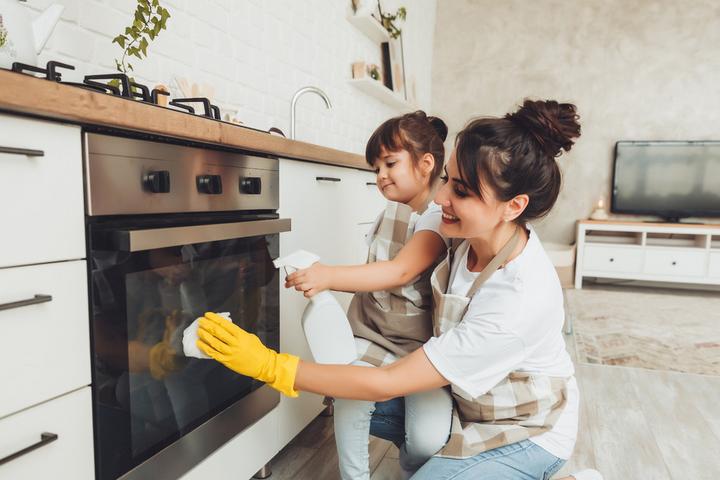 Eine Frau mit Kind putzen gemeinsam eine Backofen-Tür.