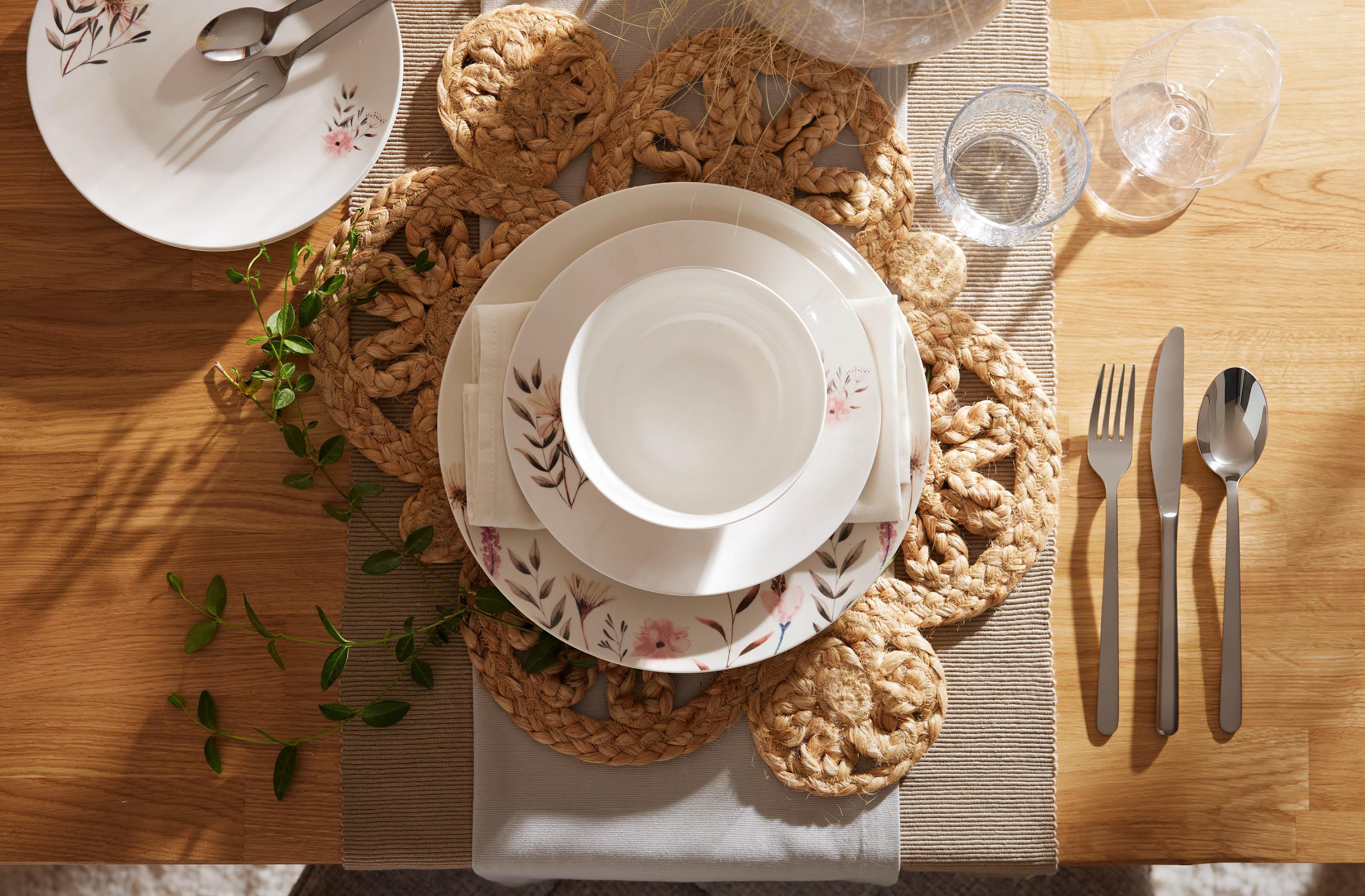 Prestretý drevený jedálenský stôl v prírodnom štýle s kvetinovým porcelánom, jutovým prestieraním a elegantným príborom pre útulnú atmosféru.