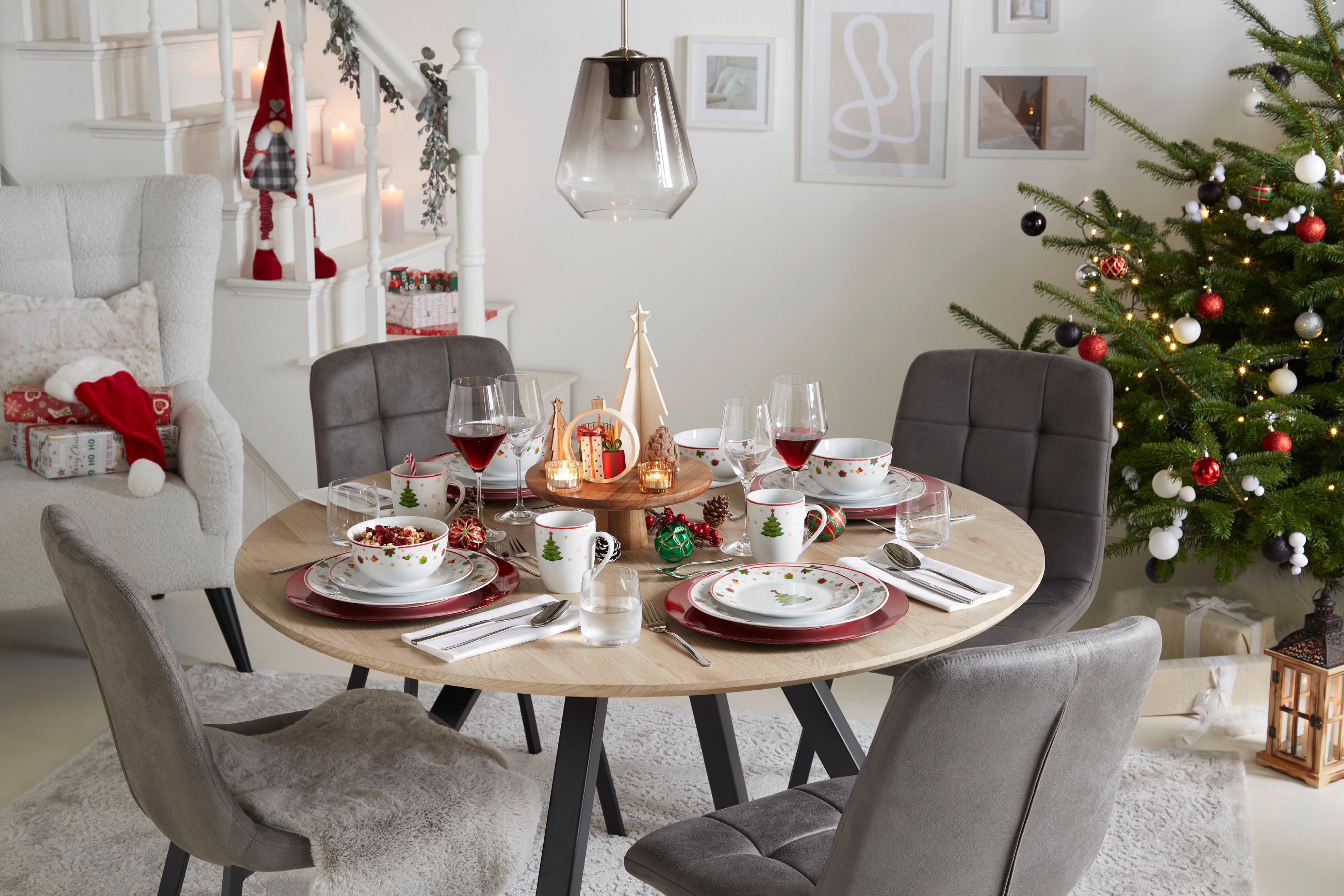 Weihnachtlich gedeckter Tisch mit Christbaum im Hintergrund.