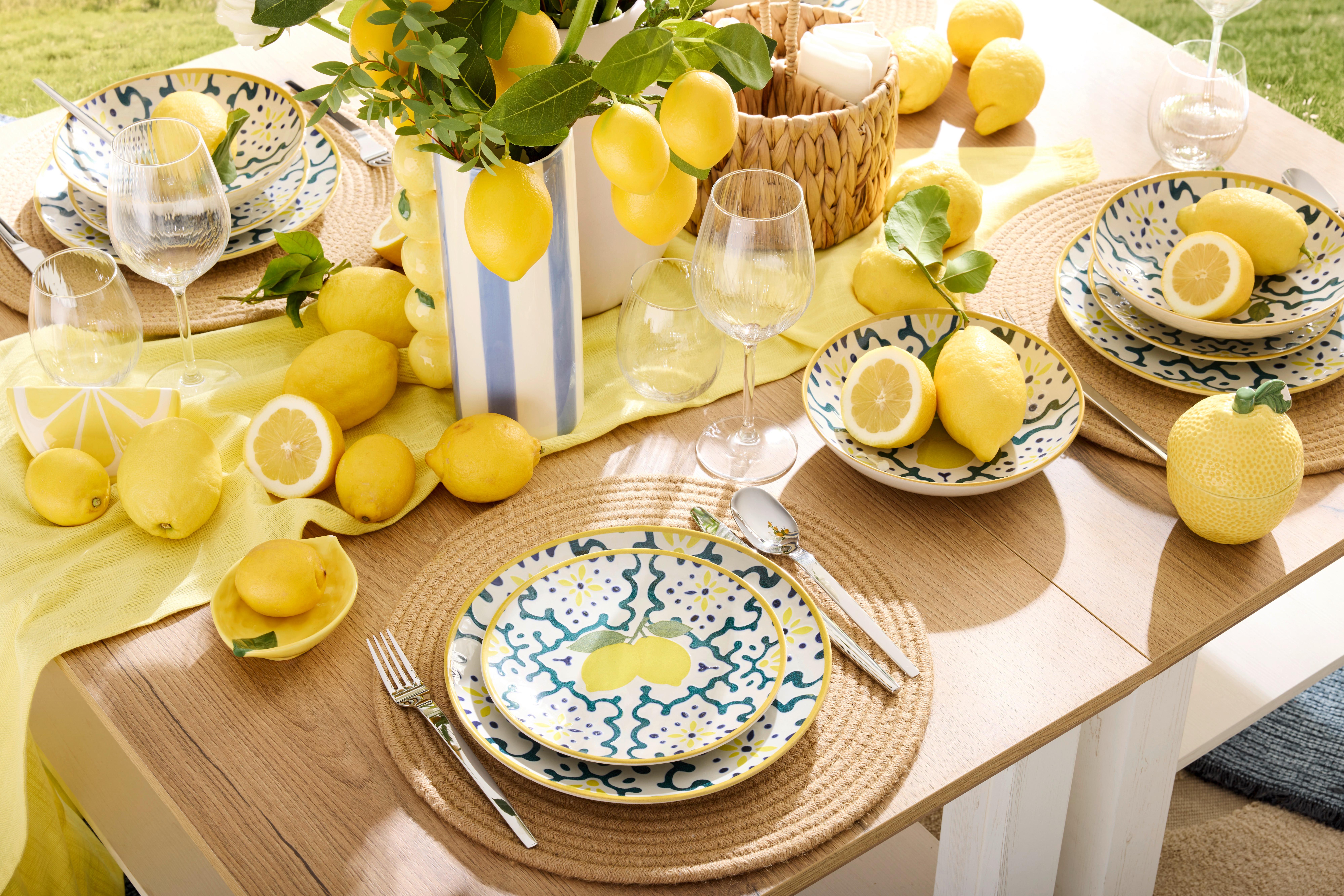 Letní prostírání s keramickým servisem Lemons, jutovými prostíráními a čerstvými citróny na slunném zahradním stole.