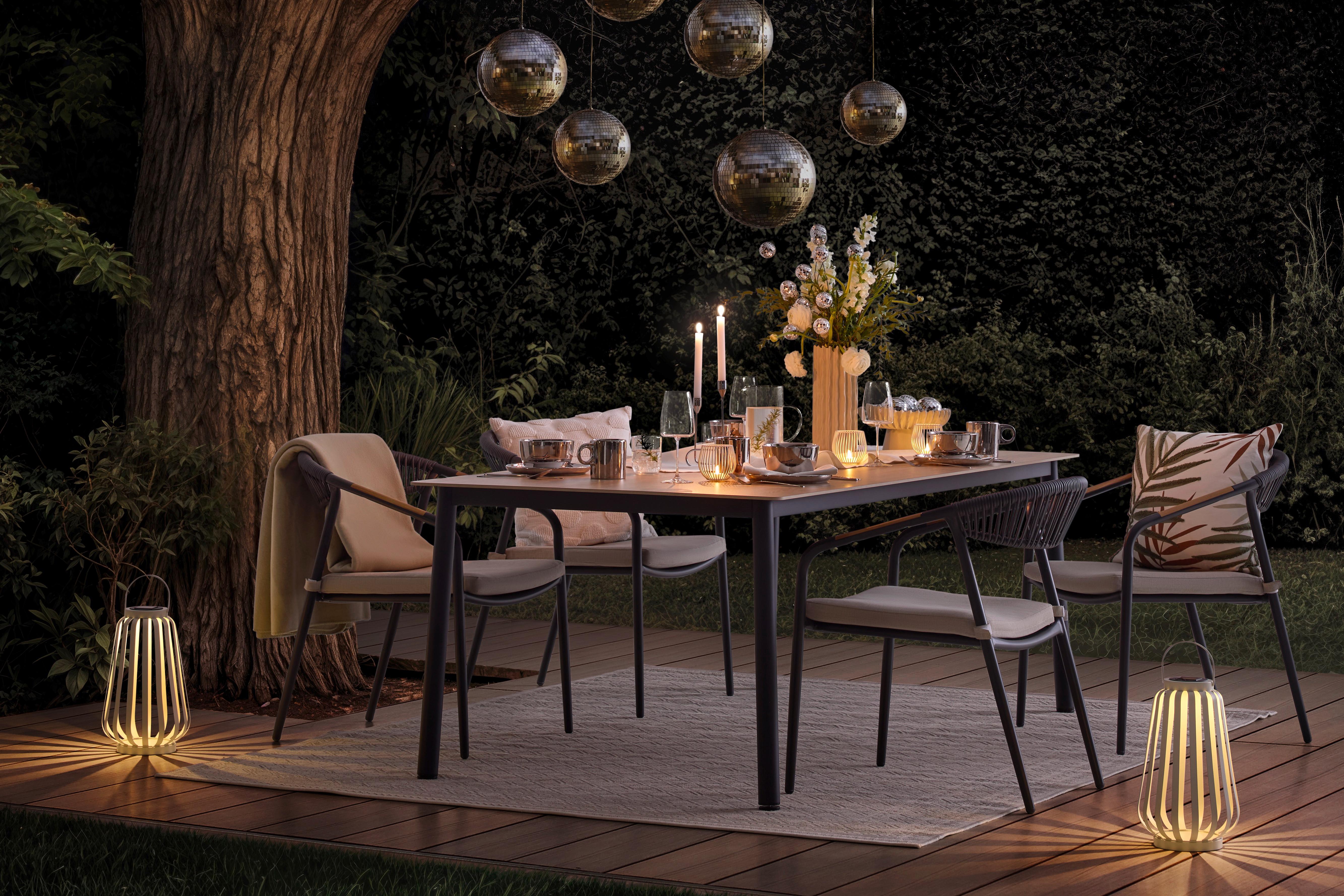 Večerné stolovanie na terase pod stromom, s jemným osvetlením, sviečkami a zrkadlovými guľami, ktoré vytvárajú útulnú atmosféru v zeleni.