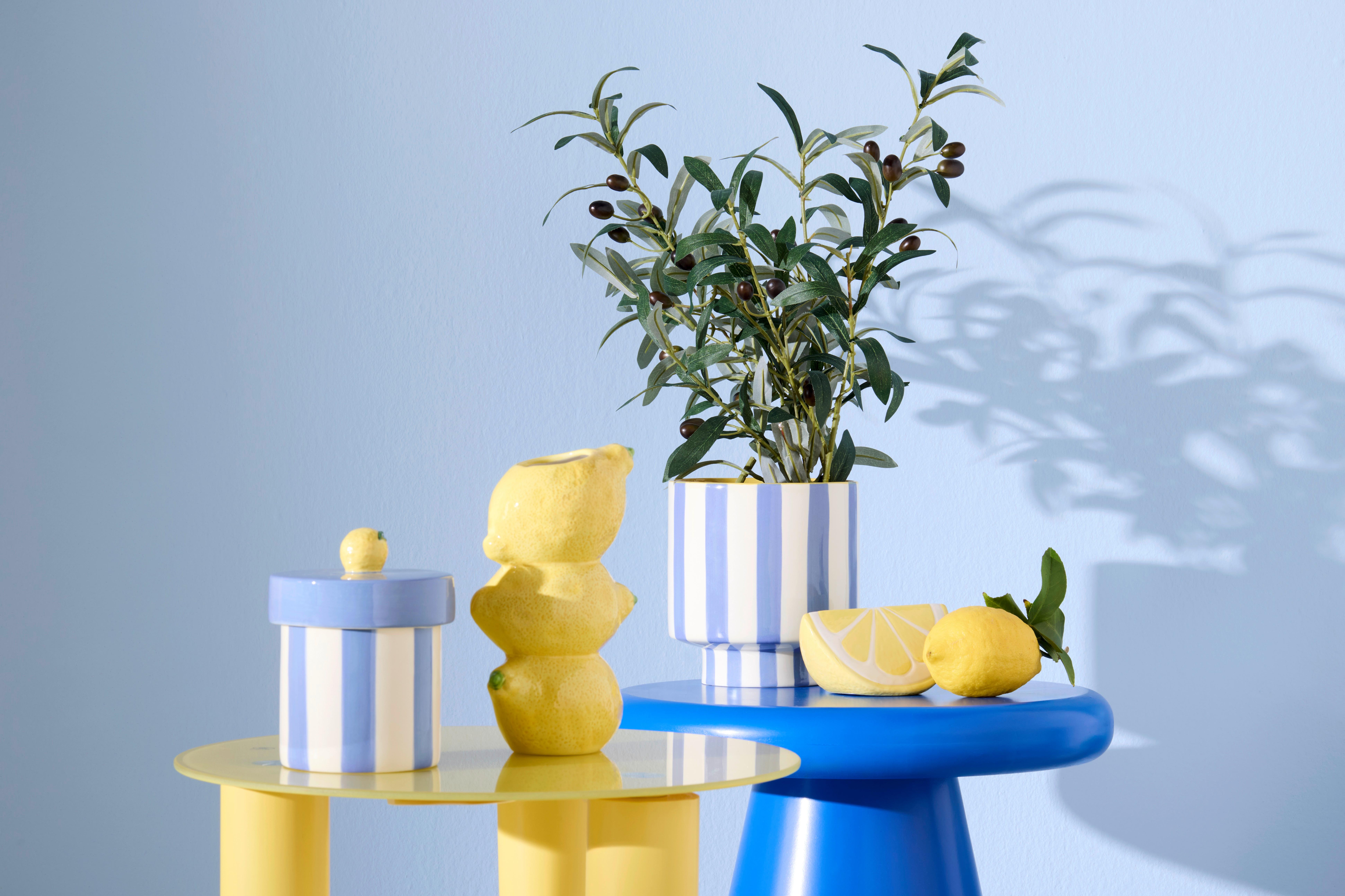 Dekorační váza Geta ve tvaru citronu, pruhovaná dekodóza Lilo a květináč Agi s olivovou větvičkou na barevných bočních stolcích Marino a Largo ve žlutomodré kombinaci.