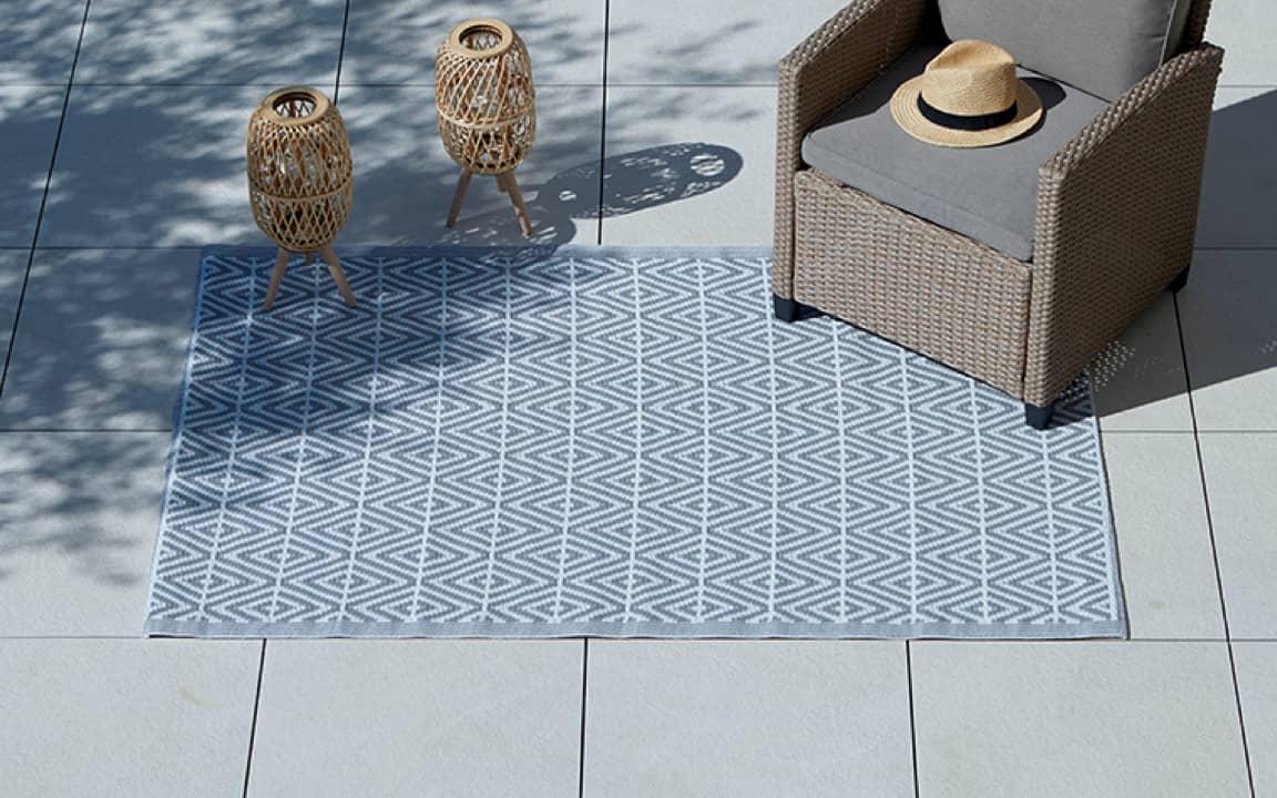 Ein Blauer Outdoorteppich auf dem ein Stuhl aus Rattan steht