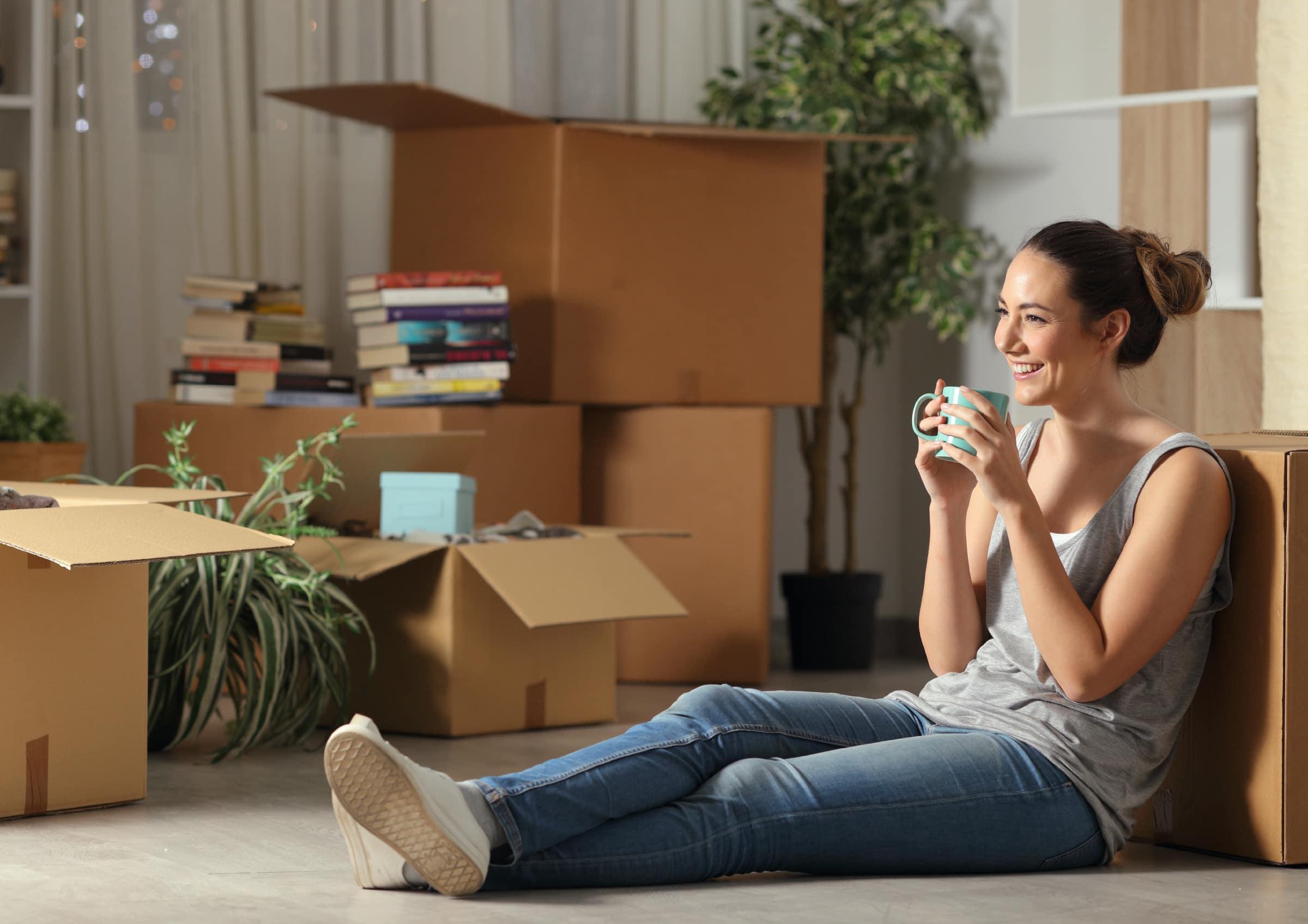 Person sitzend mit Tasse in der Hand an Kartonbox gelehnt