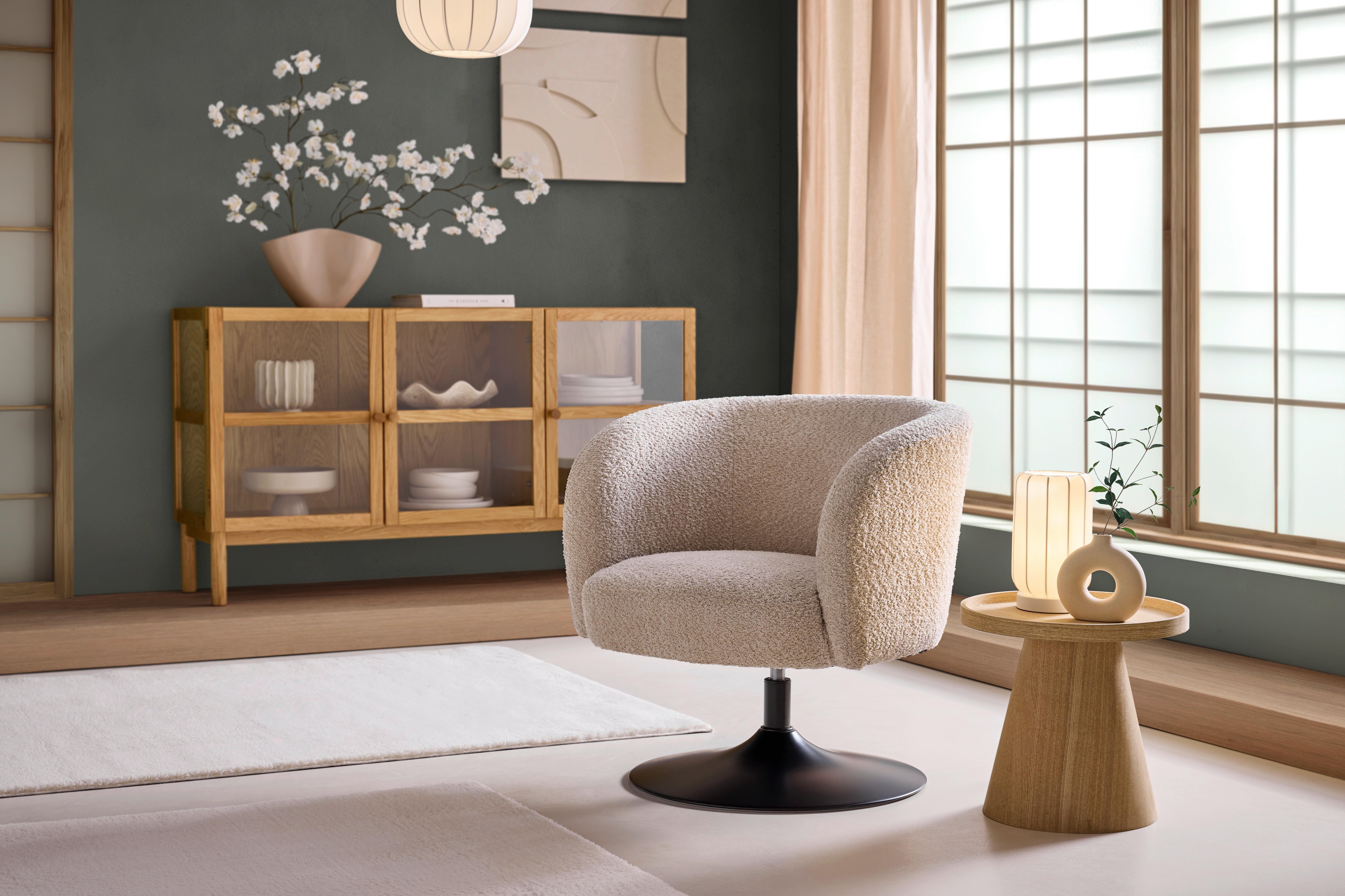 Béžové otočné kreslo v minimalistickom interiéri v štýle Japandi s drevenou komodou a príručným stolíkom.