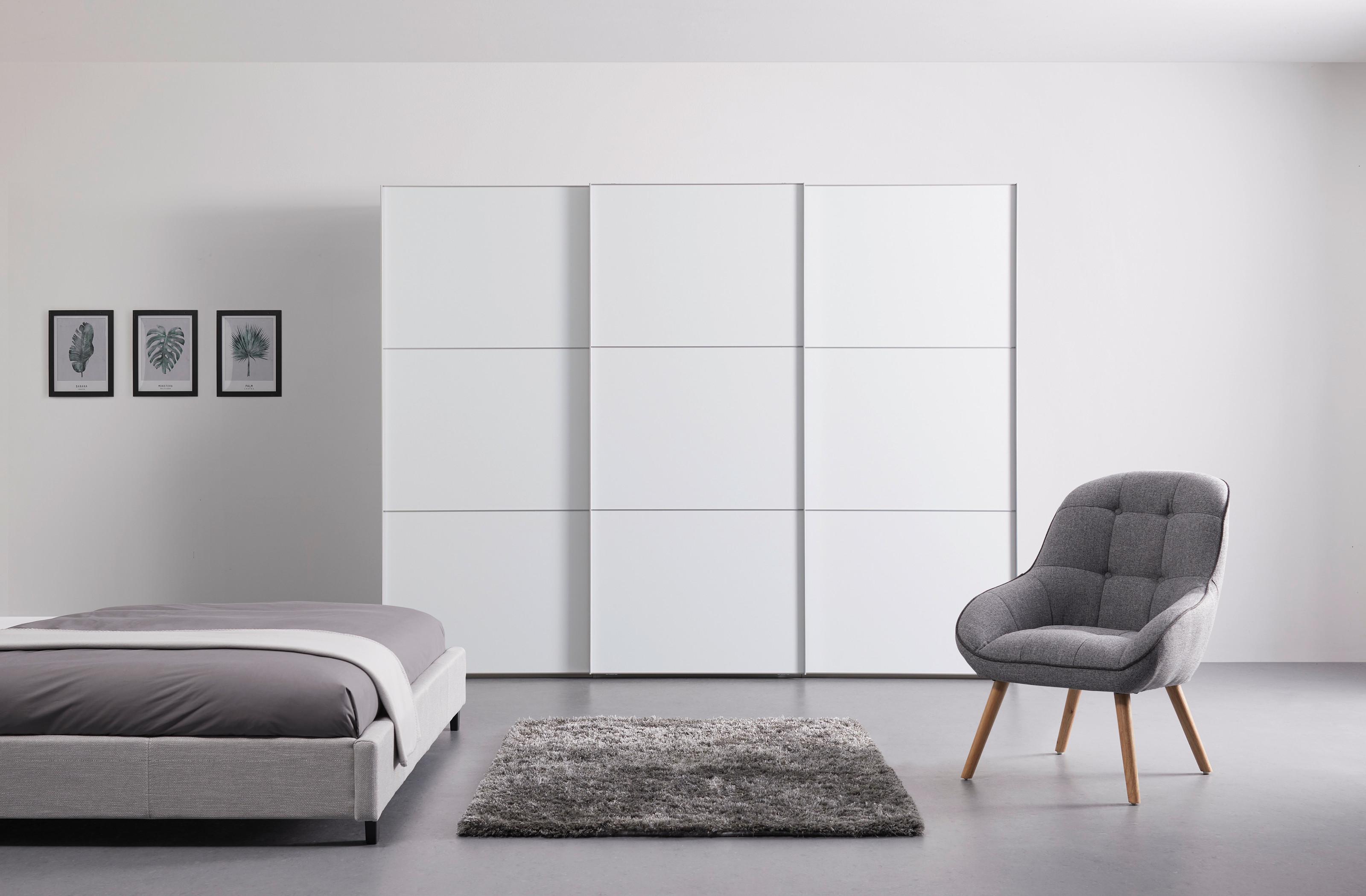 biela skriňa v minimalistickej spálni so sivou posteľou a kreslom