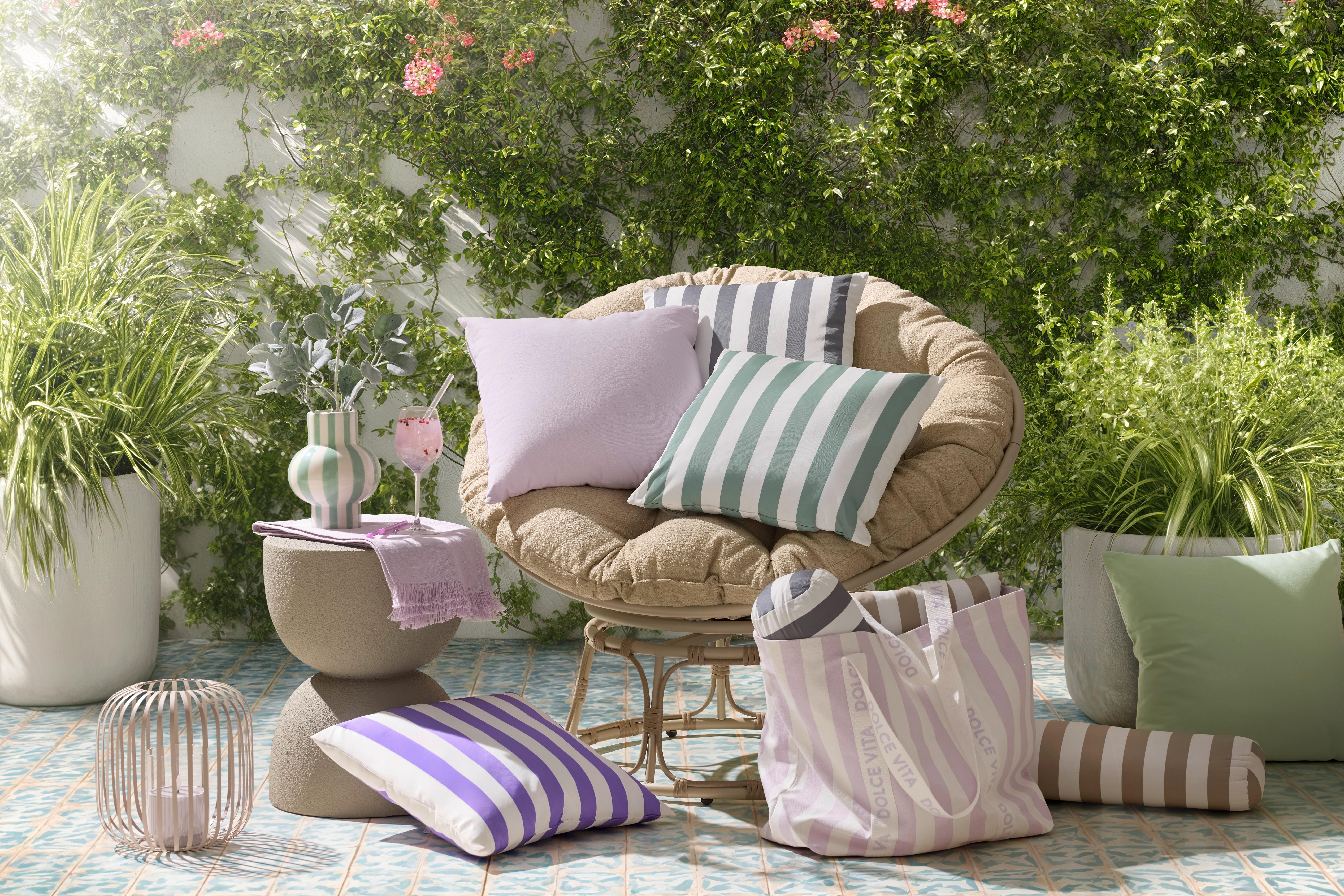 Pohodlné papasan kreslo na terase s pruhovanými outdoor vankúšmi, príručným stolíkom a doplnkami pre letný oddych v záhrade.