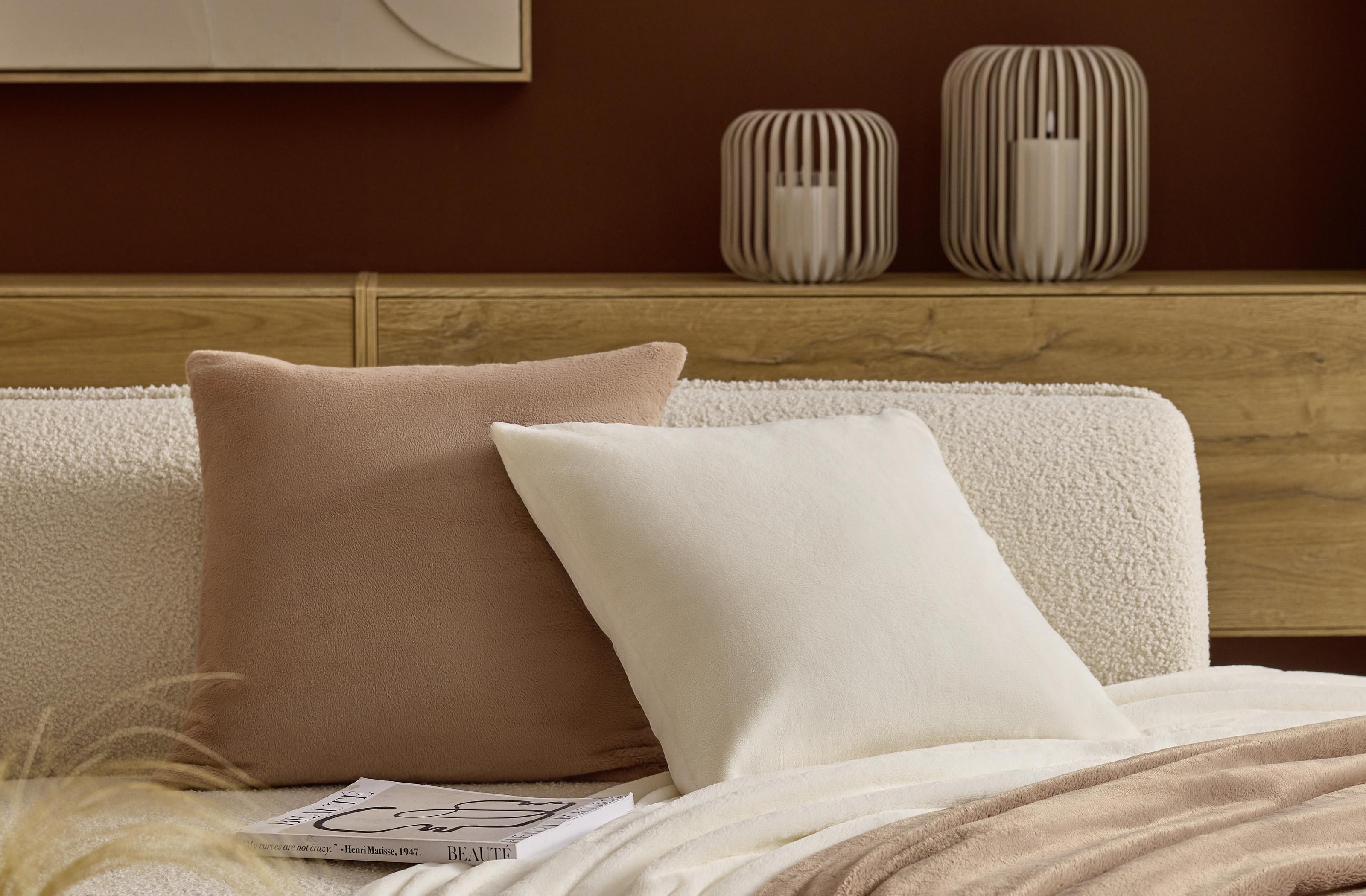 Detailní pohled na dekorace v ložnici: jemné polštáře v přírodních odstínech, dřevěná komoda a moderní svícny. Elegantní detaily, které dodávají prostoru útulnost a styl.