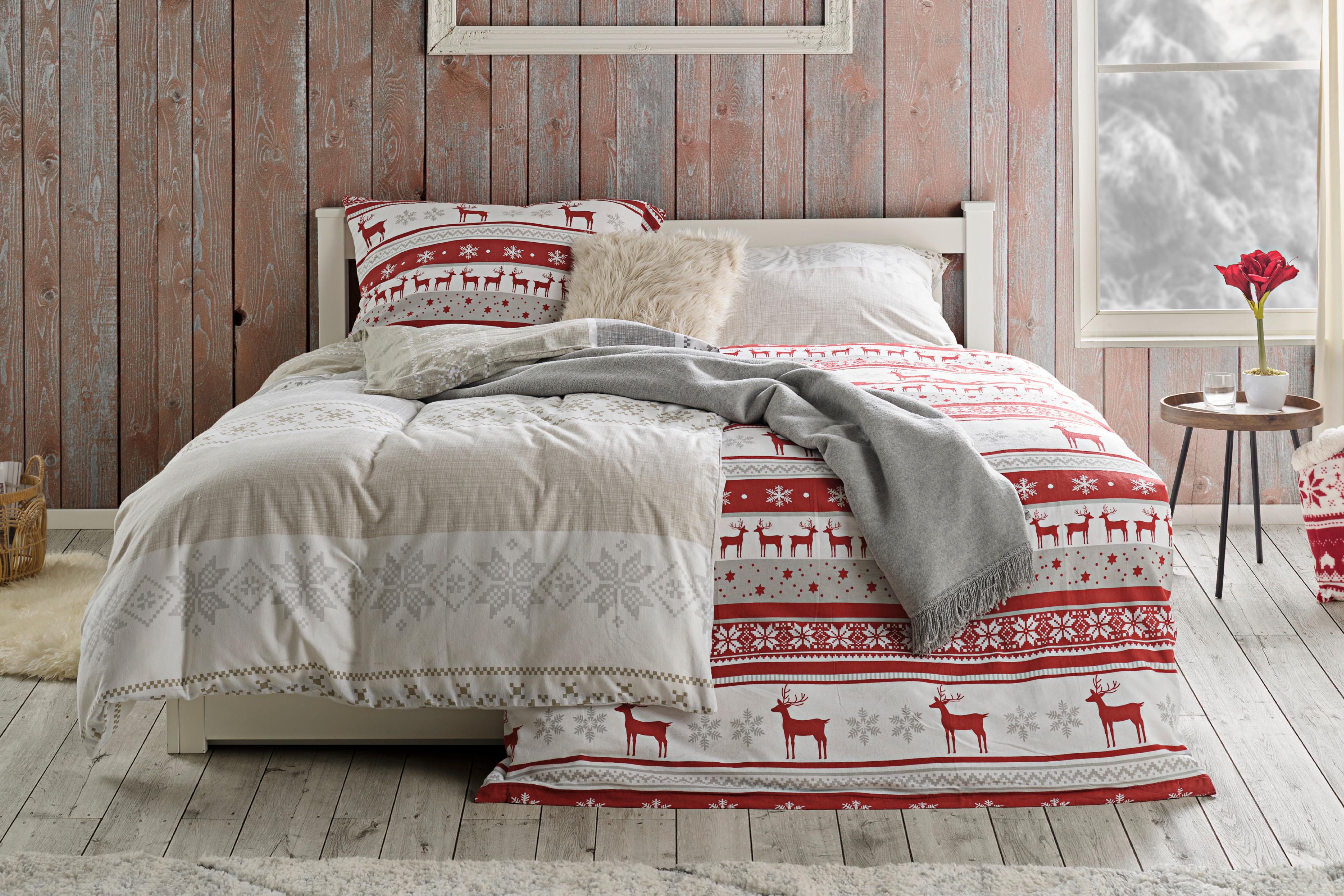 Weihnachliche, rote und beige Bettwäsche auf einem Bett vor einer Holzwand.