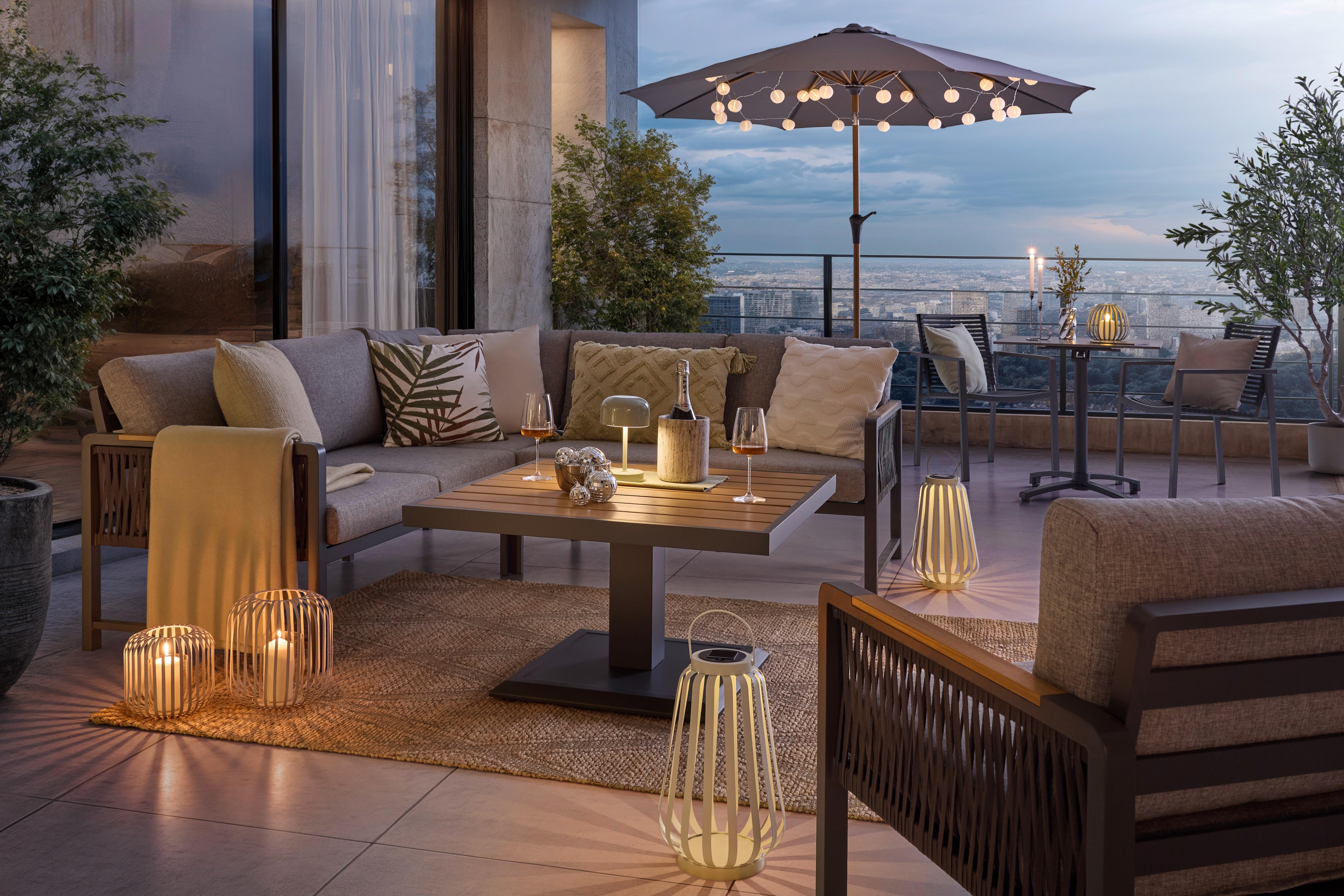 Večerná terasa s pohodlnou lounge zostavou, teplým osvetlením a sviečkami pod slnečníkom.