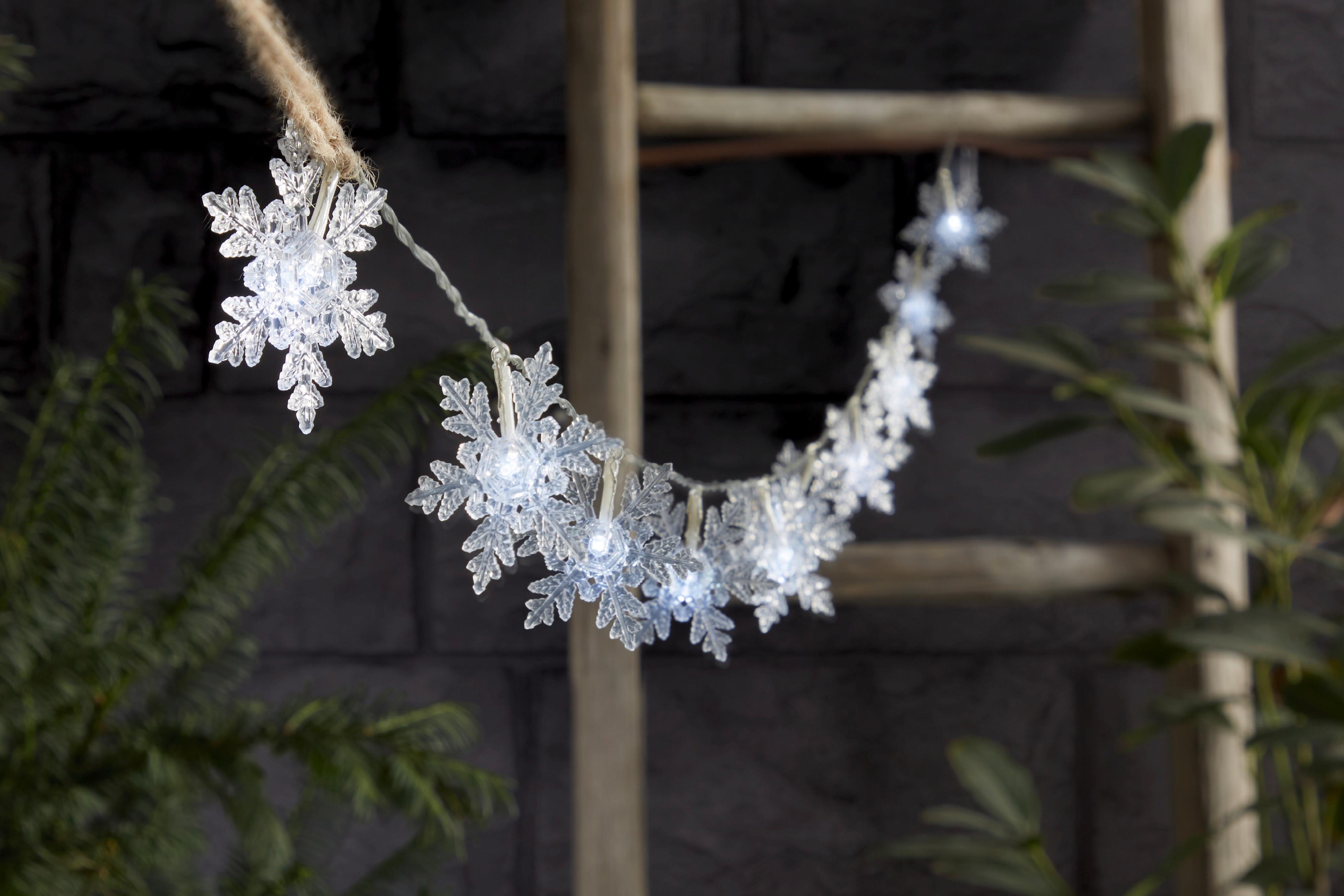Weihnachtliche Lichterkette in Form von Schneeflocken vor einer dunklen Wand.