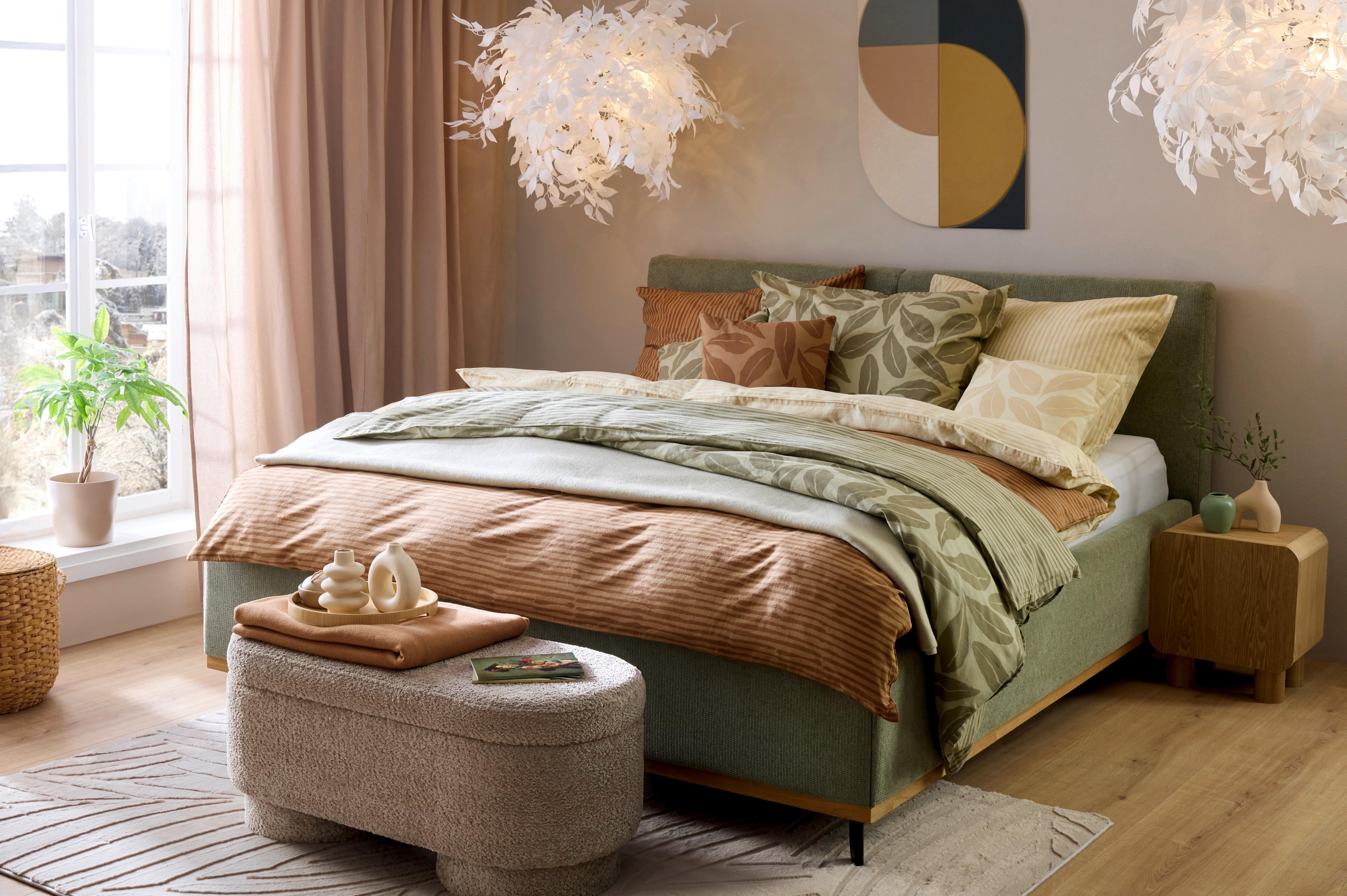 Spálňa Urban Nature so zelenou posteľou, zemitými textíliami a vankúšmi s listovým motívom.