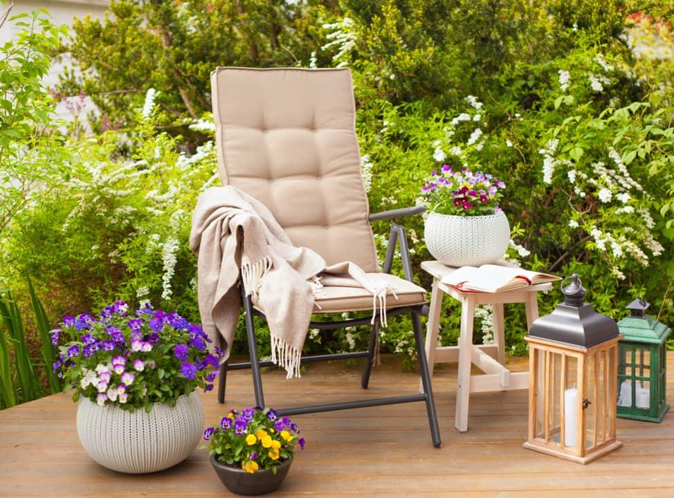Polsterstuhl mit Decke und bunten Blumen auf Terasse