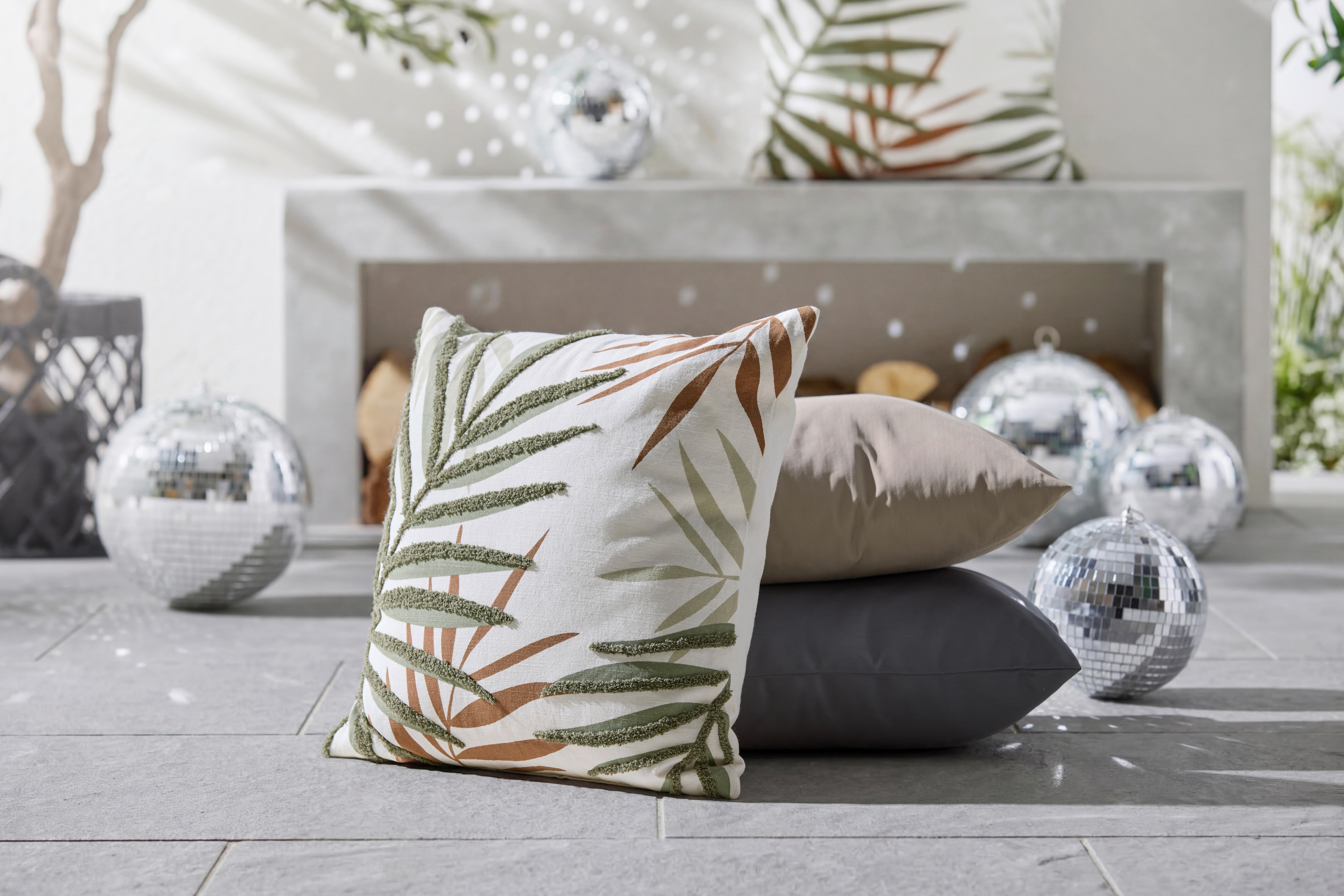 Dekoračné vankúše s listovým motívom na terase pri krbe, doplnené zrkadlovými guľami pre letnú atmosféru.
