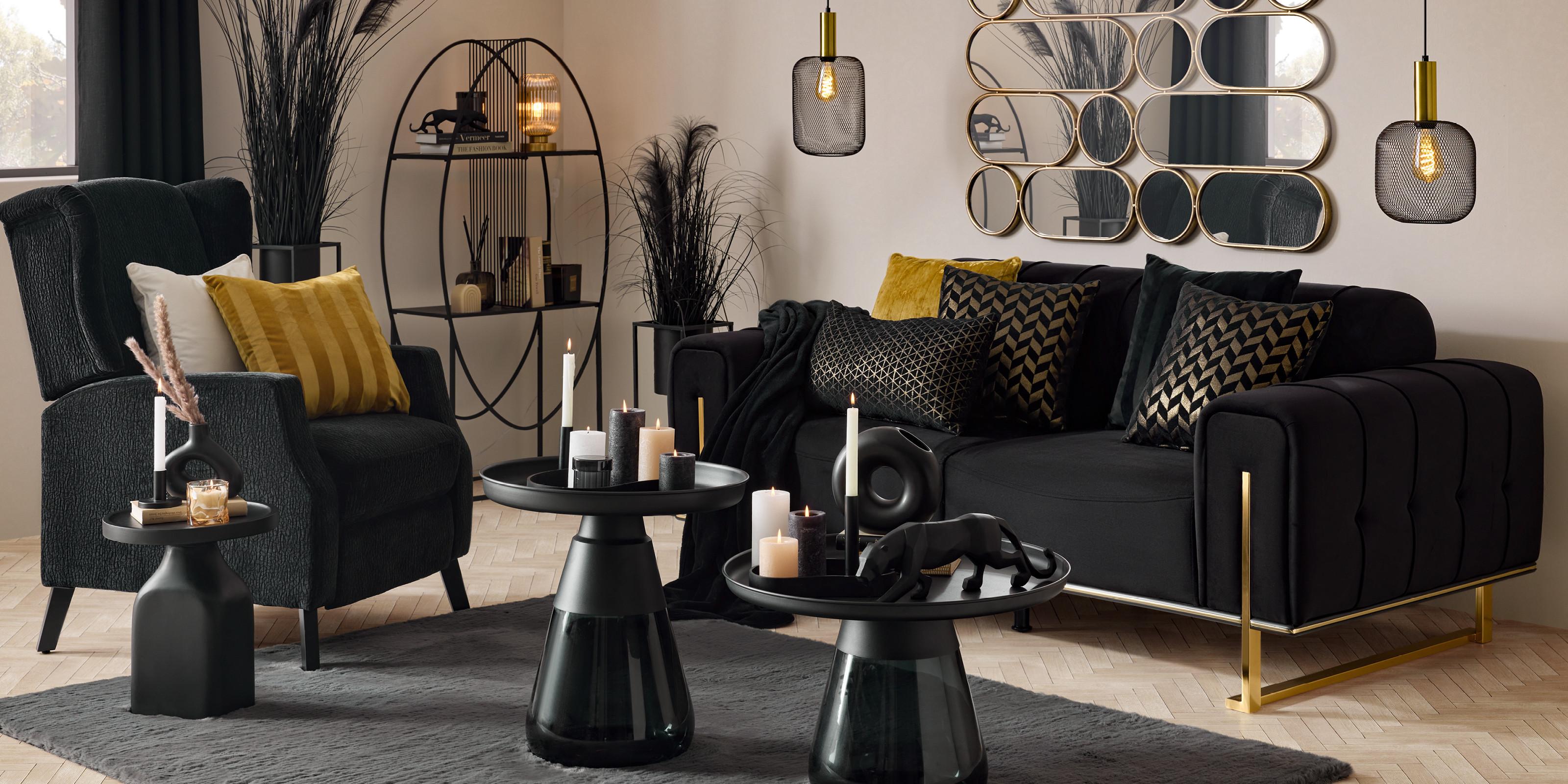 Luxusná obývačka v štýle Golden Dreams: čierna pohovka so zlatými detailmi, elegantný kreslo s kontrastnými vankúšmi, moderné dekorácie so sviečkami a zlatými akcentmi, doplnené štýlovým zrkadlom a čiernym kobercom.