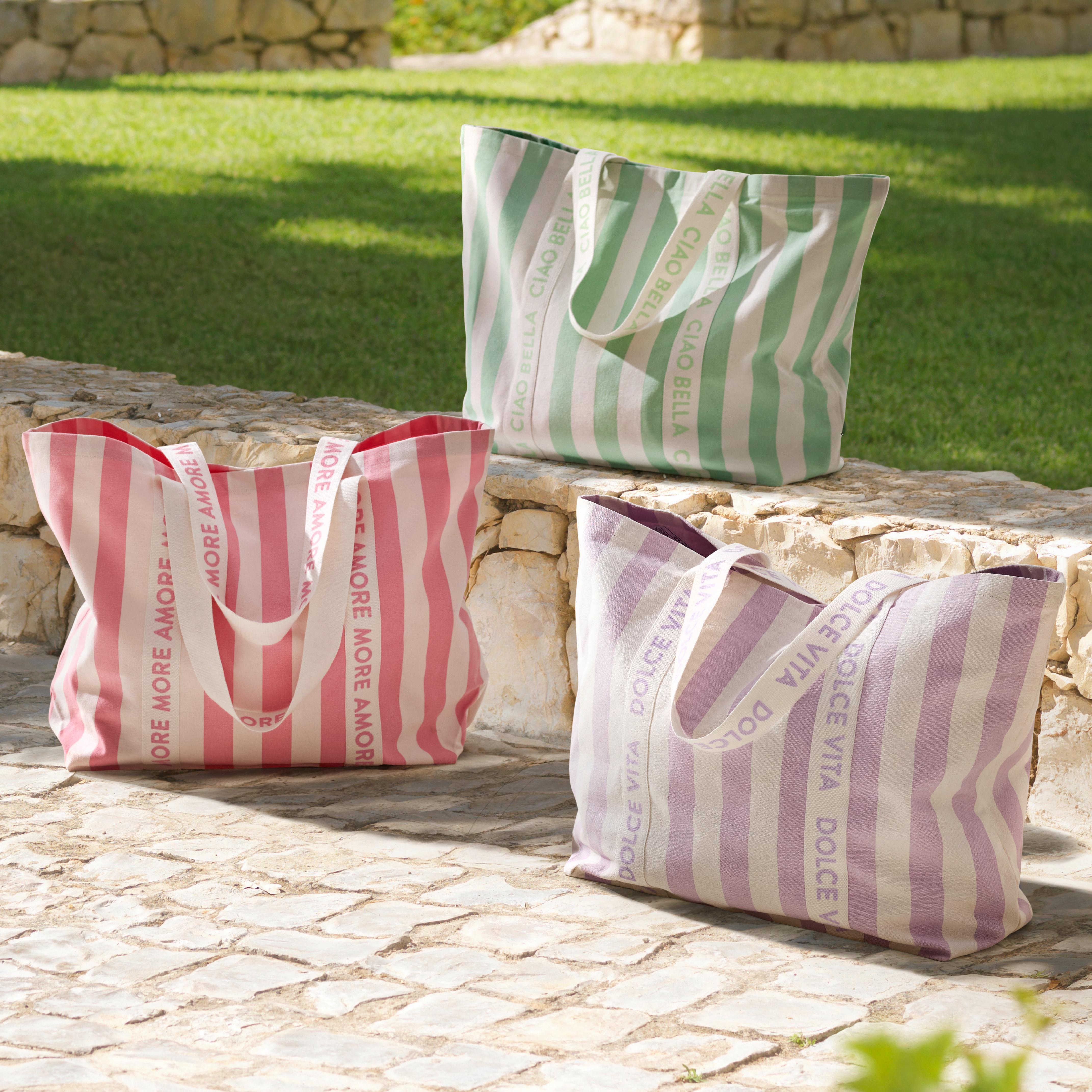 Tri pruhované plážové tašky v pastelových farbách položené na kamennej terase pri trávniku.