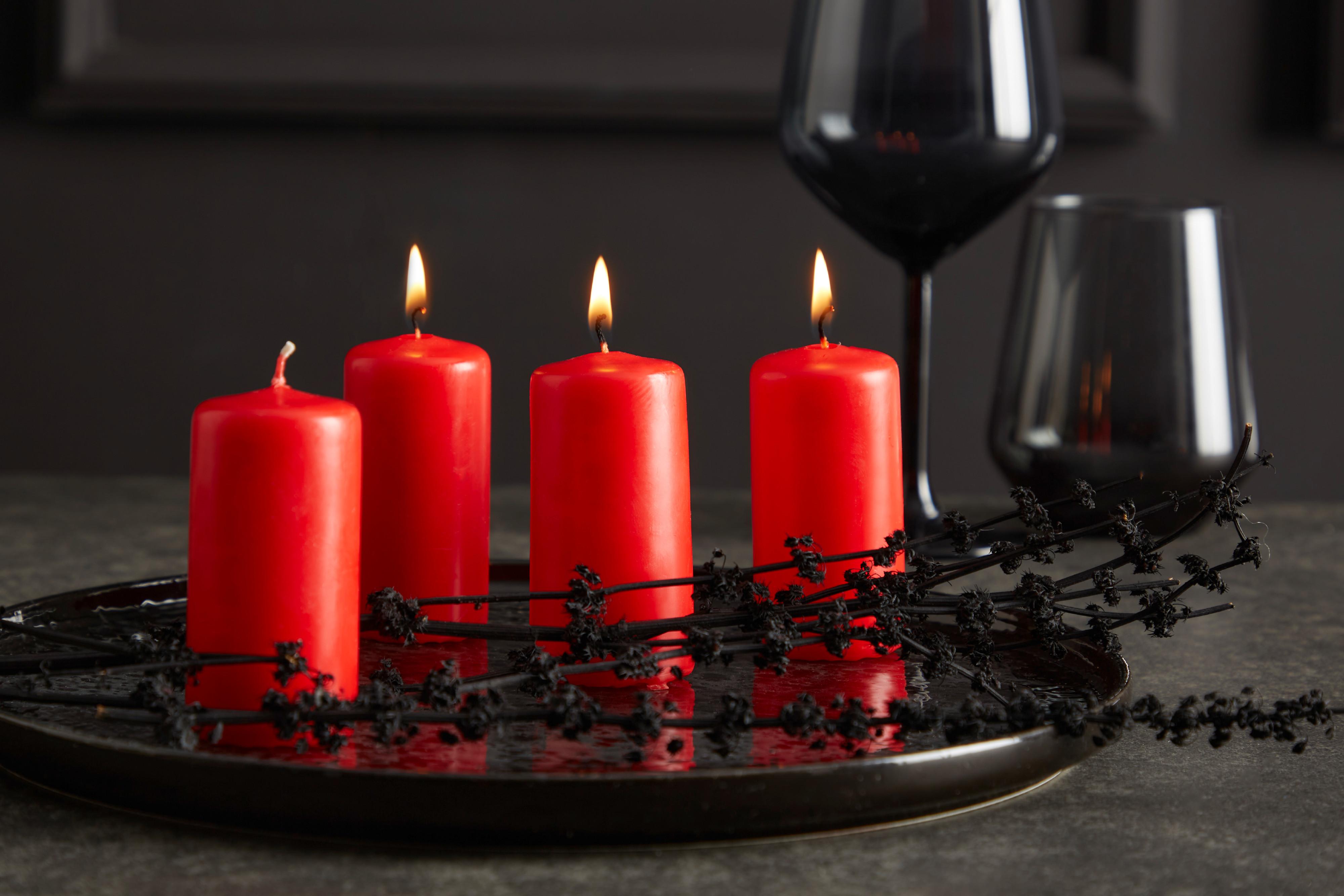 Rote Kerzen auf einem schwarzen Kerzenteller mit schwarzen Gläsern im Hintergrund.