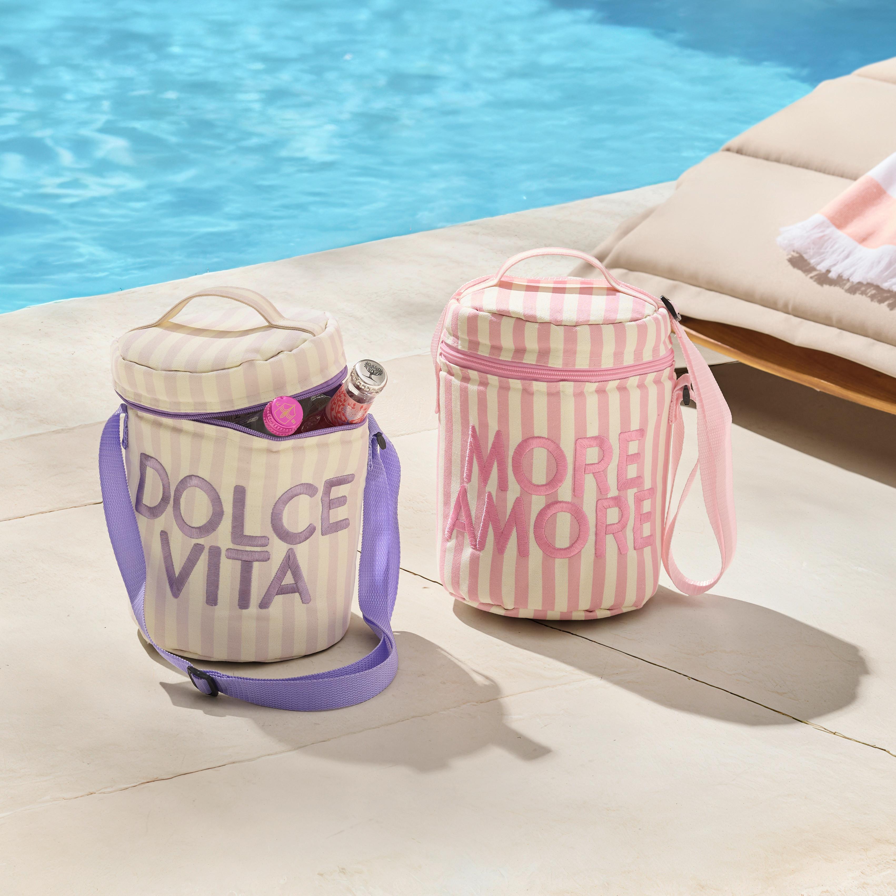 Dve pruhované chladiace tašky s popruhmi a nápismi Dolce Vita a More Amore stoja pri bazéne vedľa záhradného ležadla.
