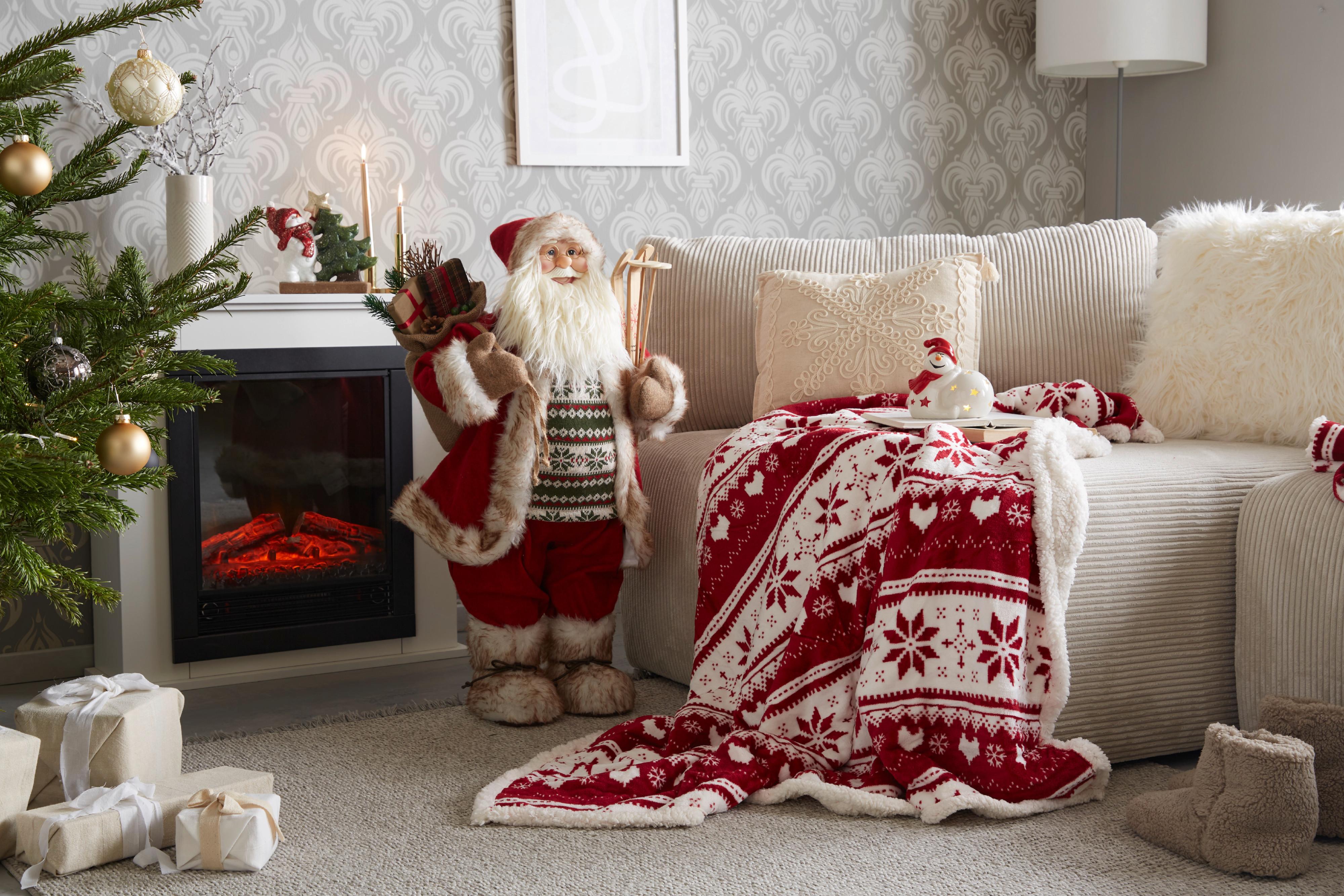 Weihnachtsmann-Figur steht zwischen Kamin und Sofa, davor steht ein Weihnachtsbaum.