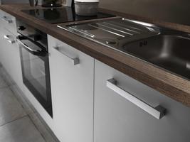 Bügelgriffe ergänzen die schlichte Optik Küche mit weißen Fronten und Arbeitsplatte in Eiche Grau Dekor